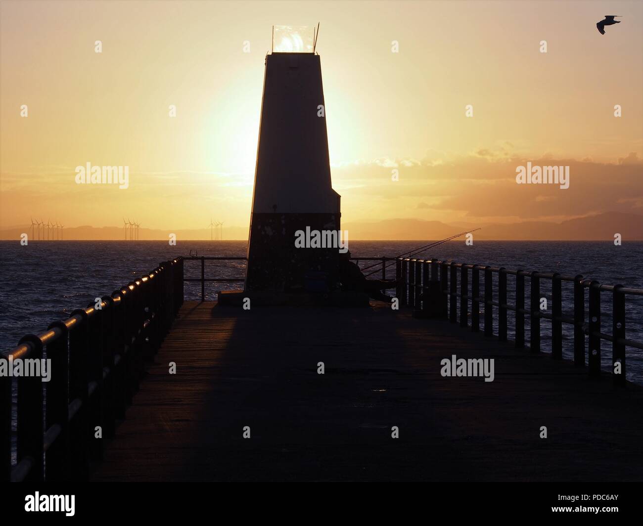 The sun setting behind the Navigation Beacon and a Sea Angler, Maryport Harbour, Cumbria, United Kingdom Stock Photo