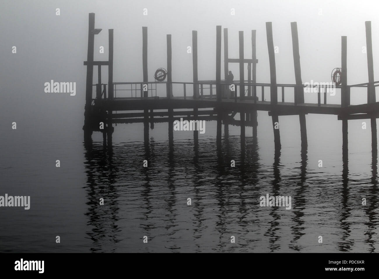A mist-covered jetty is reflected in the calm waters of Walvis Bay, Namibia, in this monochrome image. Stock Photo