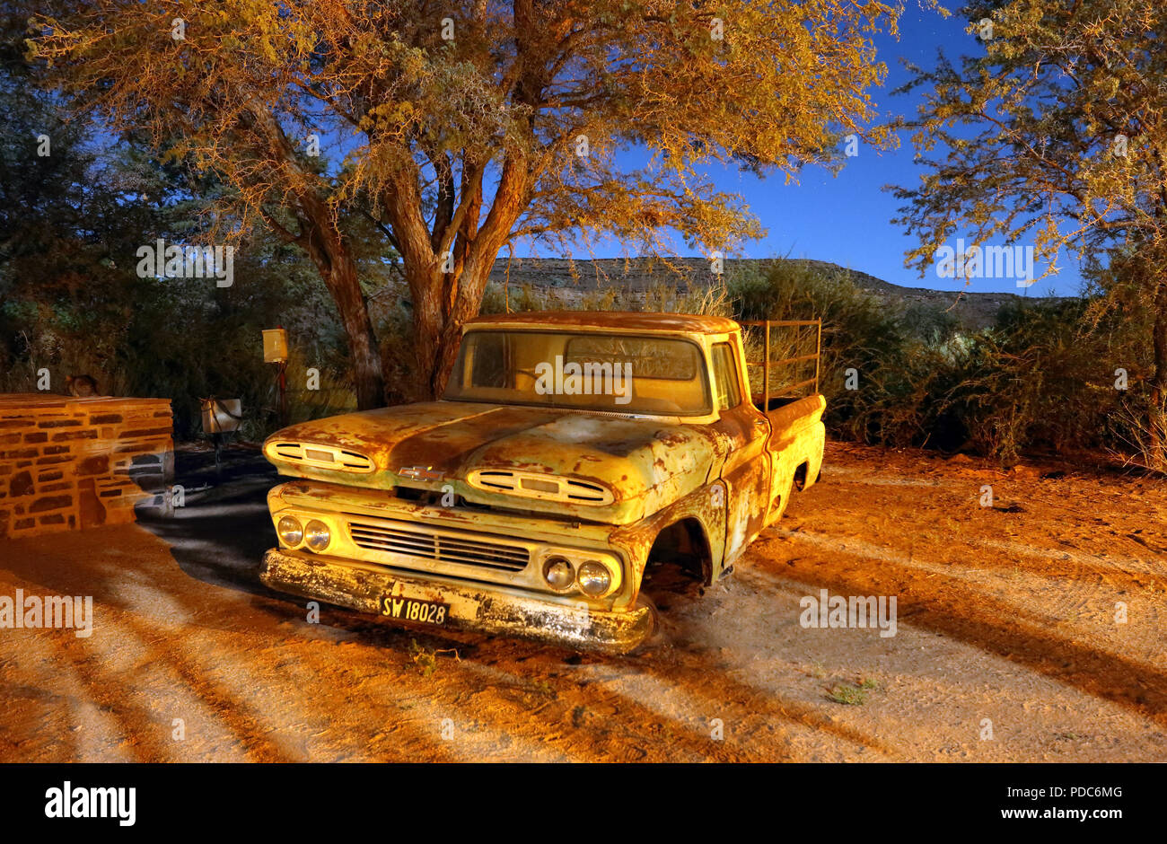 A wrecked 1960s Chevrolet Apache pickup truck photographed under a mixture of artificial light and moonlight at the Canyon Roadhouse, Namibia. Stock Photo