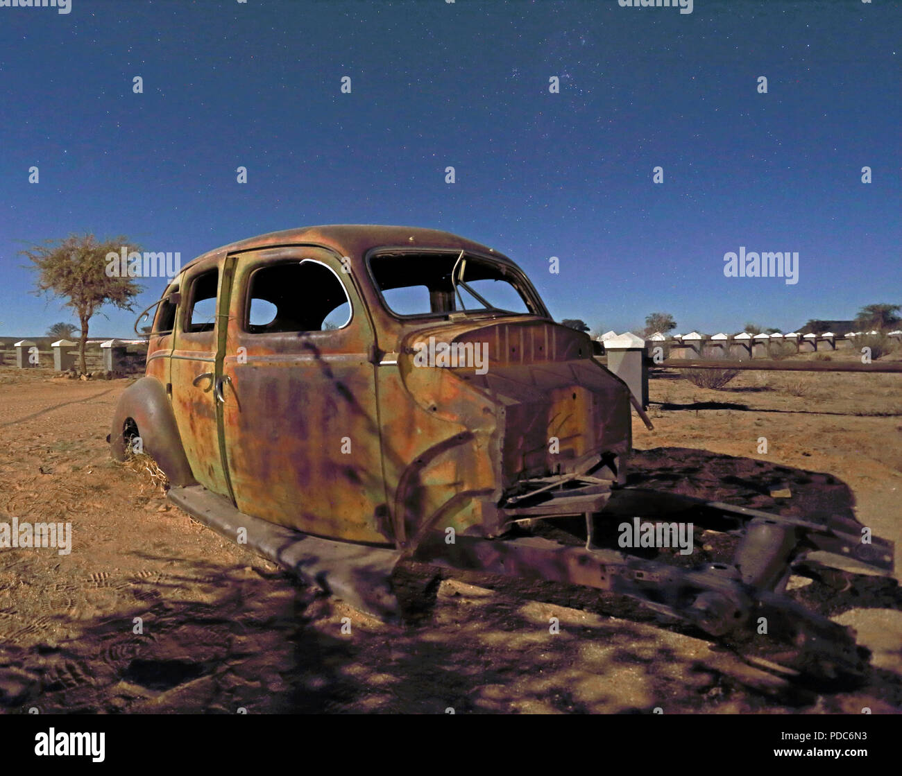 A wrecked vintage American car photographed under a mixture of artificial light and moonlight at the Canyon Roadhouse, Namibia. Stock Photo