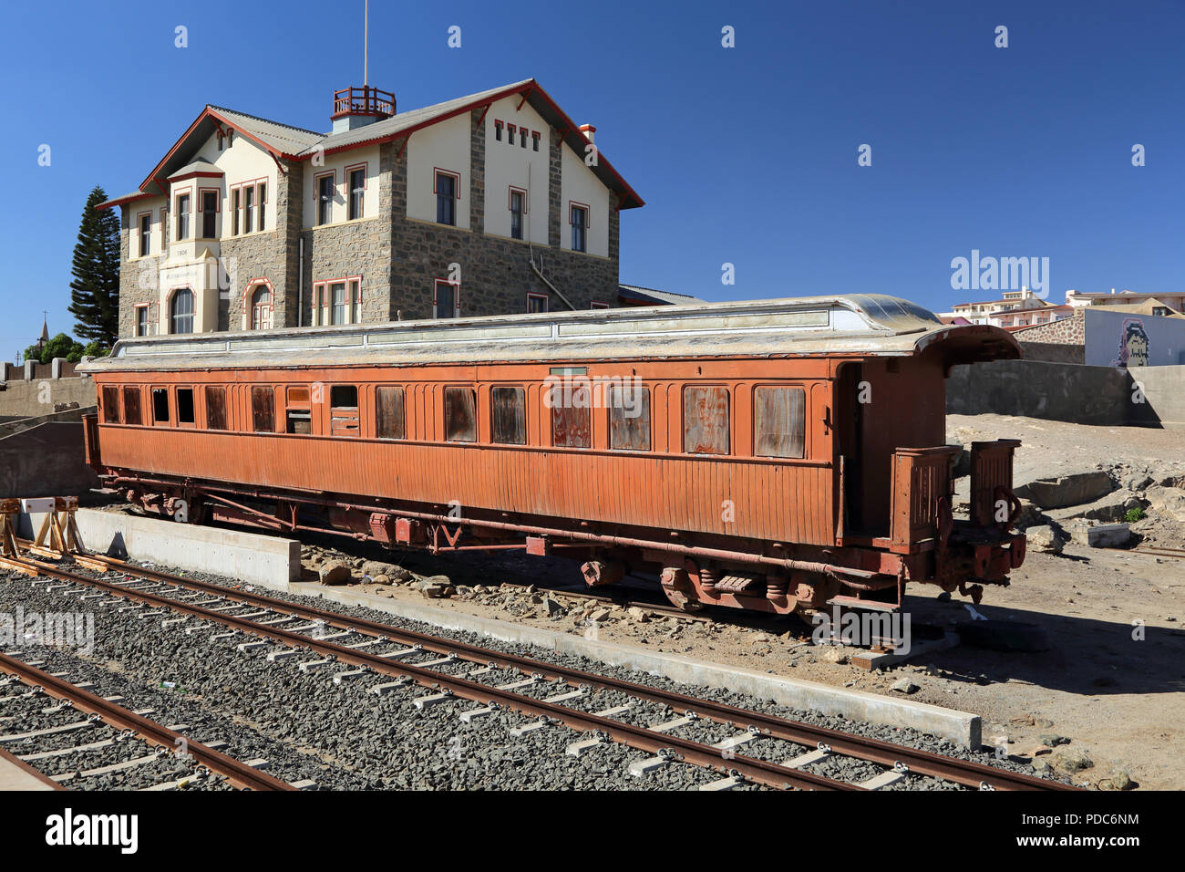 An old abandoned and disused passenger railway carriage stands in  Luderitz station, Namibia in front of historic Woermann House. Stock Photo