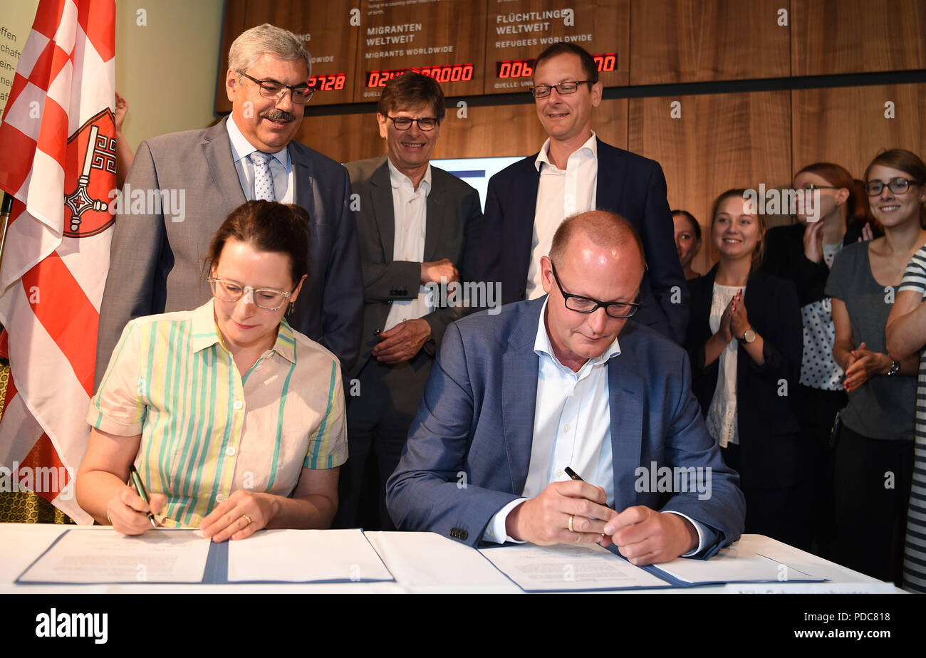 08 August 2018, Germany, Bremerhaven: Simone Eick, Managing Director of the Museum Deutsches Auswanderer Haus and Nils Schnorrenberger, Managing Director of Bremerhavener Entwicklungsgesellschaft Alter/Neuer Hafen GmbH&Co.KG, sign a contract to continue the museum's cooperation with the city of Bremerhaven until 2035. Behind them (l-r) Melf Grantz (SPD), Lord Mayor of the City of Bremerhaven, Andreas Heller, partner of Deutsches Auswandererhaus gemeinnützige GmbH, Martin Günthner (SPD), Senator for Economics, Labour and Ports, Bremen, and employees of the museum are watching. Photo: Carmen Jas Stock Photo