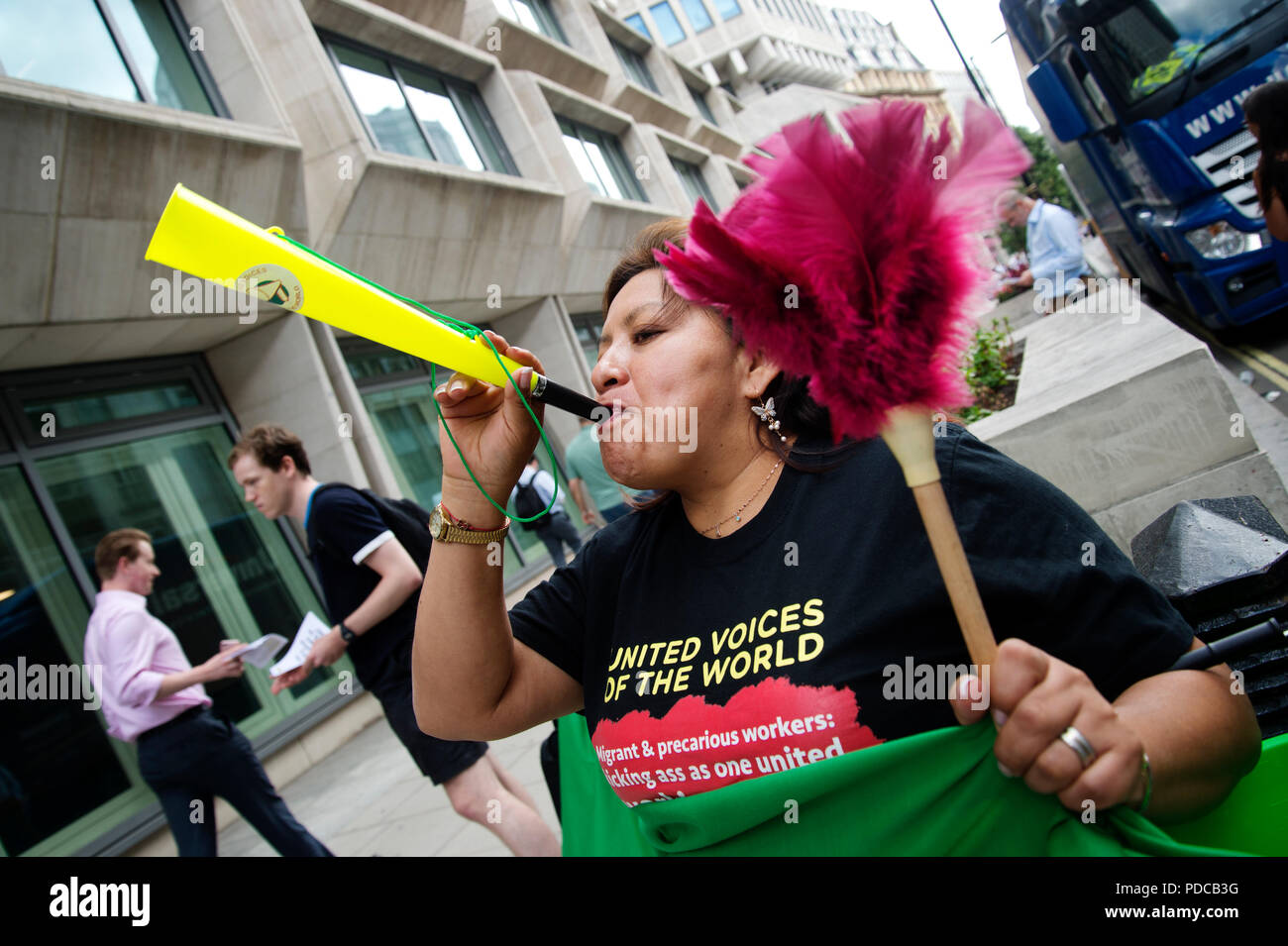 London, UK. 8th August, 2018. Ministry of Justice, Petty France, London. Cleaners from the United Voices of the World Union strike for three days demanding they be paid the London Living Wage of £10.20 an hour instead of the minimum wage of £7.83 that they currently get. A cleaner holds a feather duster and blows a vuvuzela Credit: Jenny Matthews/Alamy Live News Stock Photo