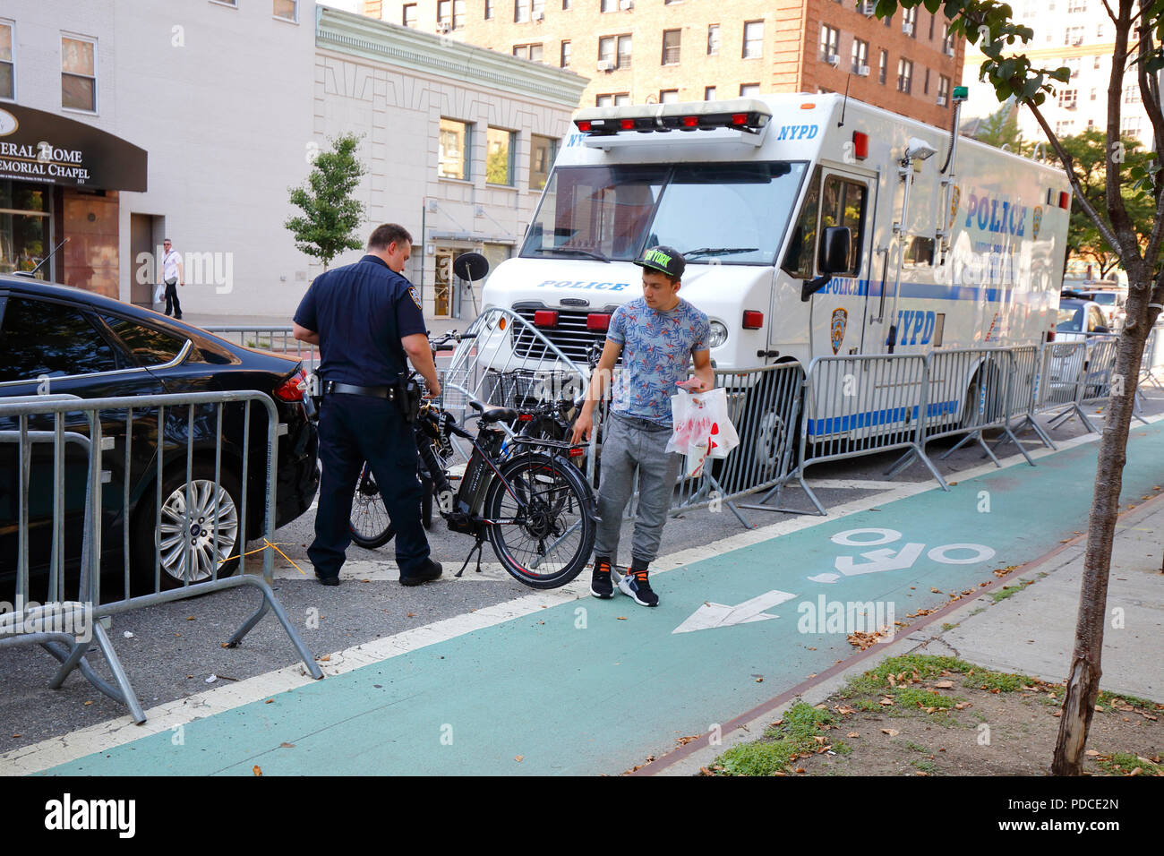 New York, NY, USA. 8th August, 2018.  Police examine a confiscated Class 2--throttle assist--electric bicycle, while a cyclist lingers briefly for a final parting touch. Electric bikes are currently illegal in New York State. NYC Mayor De Blasio has directed the Department of Transportation to begin allowing Class 1 pedal assisted electric bikes, while continuing the crackdown on all e bikes.  Most electric bike users are food delivery personnel. Stock Photo