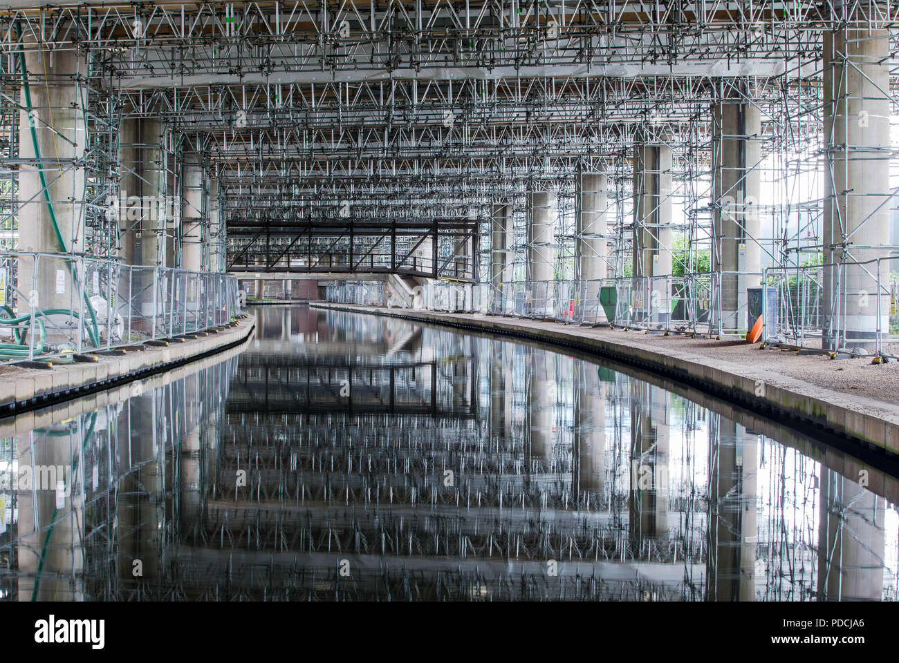 Oldbury, West Midlands, UK. 9th August, 2018. A two-year repair project on the elevated section of the M5 motorway passes its halfway mark. Scaffolding is reflected in the canal. At more than £100 million, M5 Oldbury is believed to be the largest concrete repair project, by value, ever carried out in Britain. Already more than 5,000 separate repairs have been carried out on the southbound carriageway, 3,500 more than anticipated. The Oldbury viaduct carries 120,000 vehicles a day on one of Europe's busiest motorways, and vehicles are limited to 30mph. Peter Lopeman/Alamy Live News Stock Photo