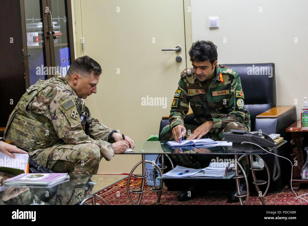 KANDAHAR PROVINCE, Afghanistan (August 5, 2018) -- U.S. Army 1st Lt. Steven Bettger, left, Train, Advise and Assist Command-South medical advisor, and Afghan Lt. Col Momand K., Kandahar Regional Military Hospital acting commander, exchange notes, August 5, 2018, during a medical advisory visit at Camp Hero in Kandahar, Afghanistan. Bettger and staff members from the Kandahar Airfield NATO Role III Multinational Medical Unit conduct routine visits to KRMH to train and advice Afghan medical staff. (U.S. Army photo by Staff Sgt. Neysa Canfield/TAAC-South Public Affairs) Stock Photo