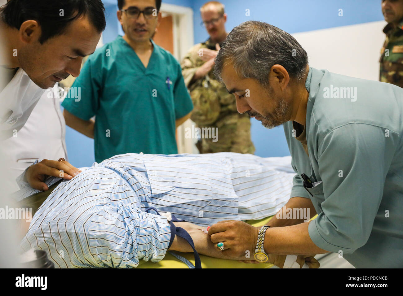 KANDAHAR PROVINCE, Afghanistan (August 5, 2018) -- Afghan radiology technicians prepare a patient for a body scan, August 5, 2018, after receiving advice from U.S. Navy Lt. Cdr. Justin S. Clark, radiology technician for Kandahar Airfield NATO Role III Multinational Medical Unit, during a medical advisory visit at Kandahar Regional Military Hospital, Camp Hero in Kandahar, Afghanistan. Staff members from the Role III conduct routine visits to KRMH to train and advice Afghan medical staff. (U.S. Army photo by Staff Sgt. Neysa Canfield/TAAC-South Public Affairs) Stock Photo