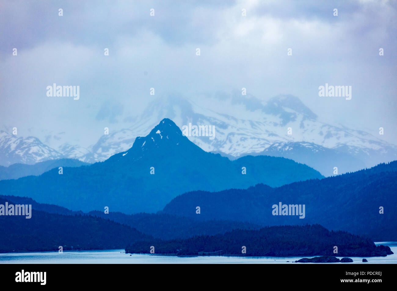 Snow capped rugged rocky mountains in clouds across Kachemak Bay from Home on Alaska’s Kenai Peninsula in Homer Alaska Stock Photo