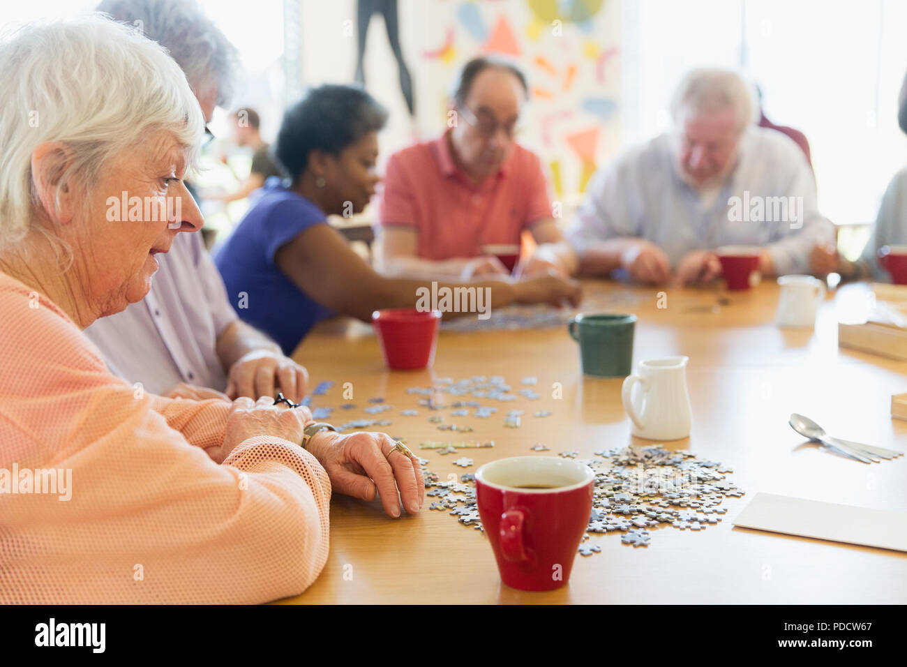 Senior woman assembling jigsaw puzzle with friends at table in community center Stock Photo