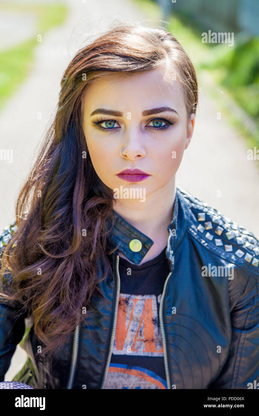 An alternative looking girl sitting down outside wearing a bikers leather jacket. Stock Photo