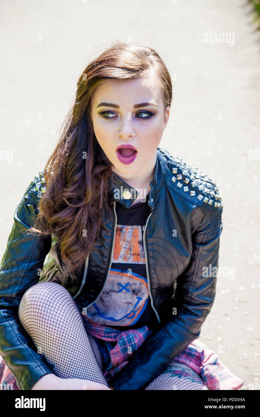 An alternative looking girl sitting down outside wearing a bikers leather jacket. Stock Photo