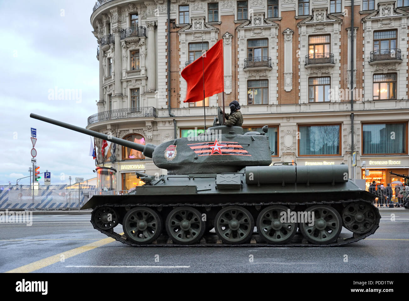 = Legendary T-34 Tank with Waving Red Banner =  Soviet T-34 tank with waving red banner at the beginning of Tverskaya street in the background of hote Stock Photo