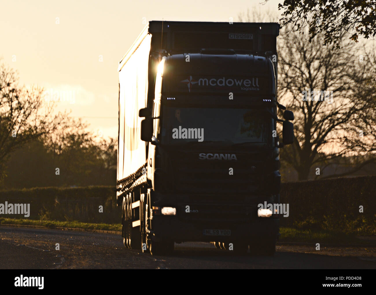 Scania HGV on A-road silhouetted by sun Stock Photo