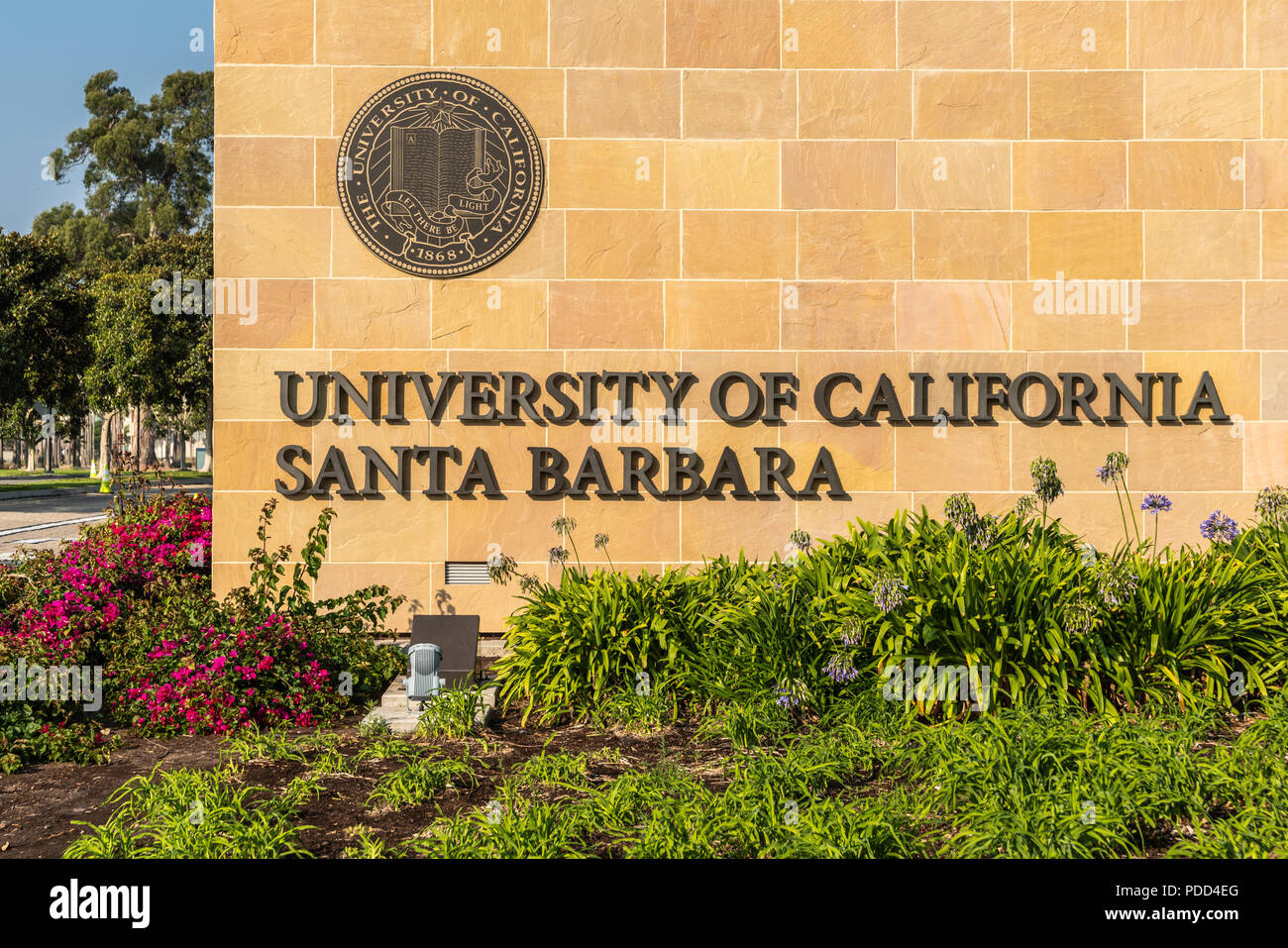 Goleta, California, USA - August 7, 2018: Closeup of name and seal of UCSB at Monumental brown stone Henley Gate. Plenty of grass and flowers up front Stock Photo