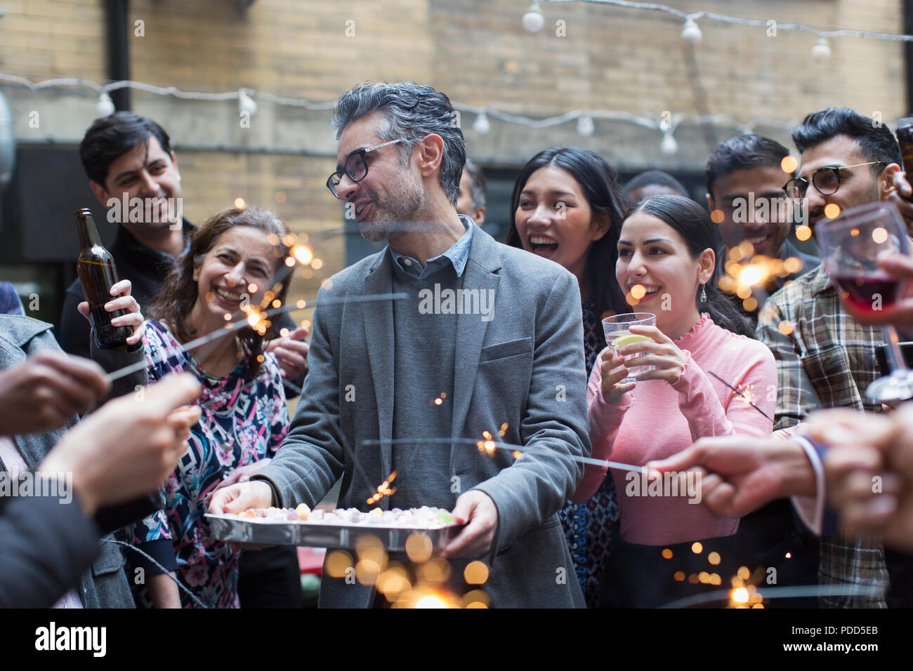 Friends with sparklers celebrating with man holding birthday cake Stock Photo