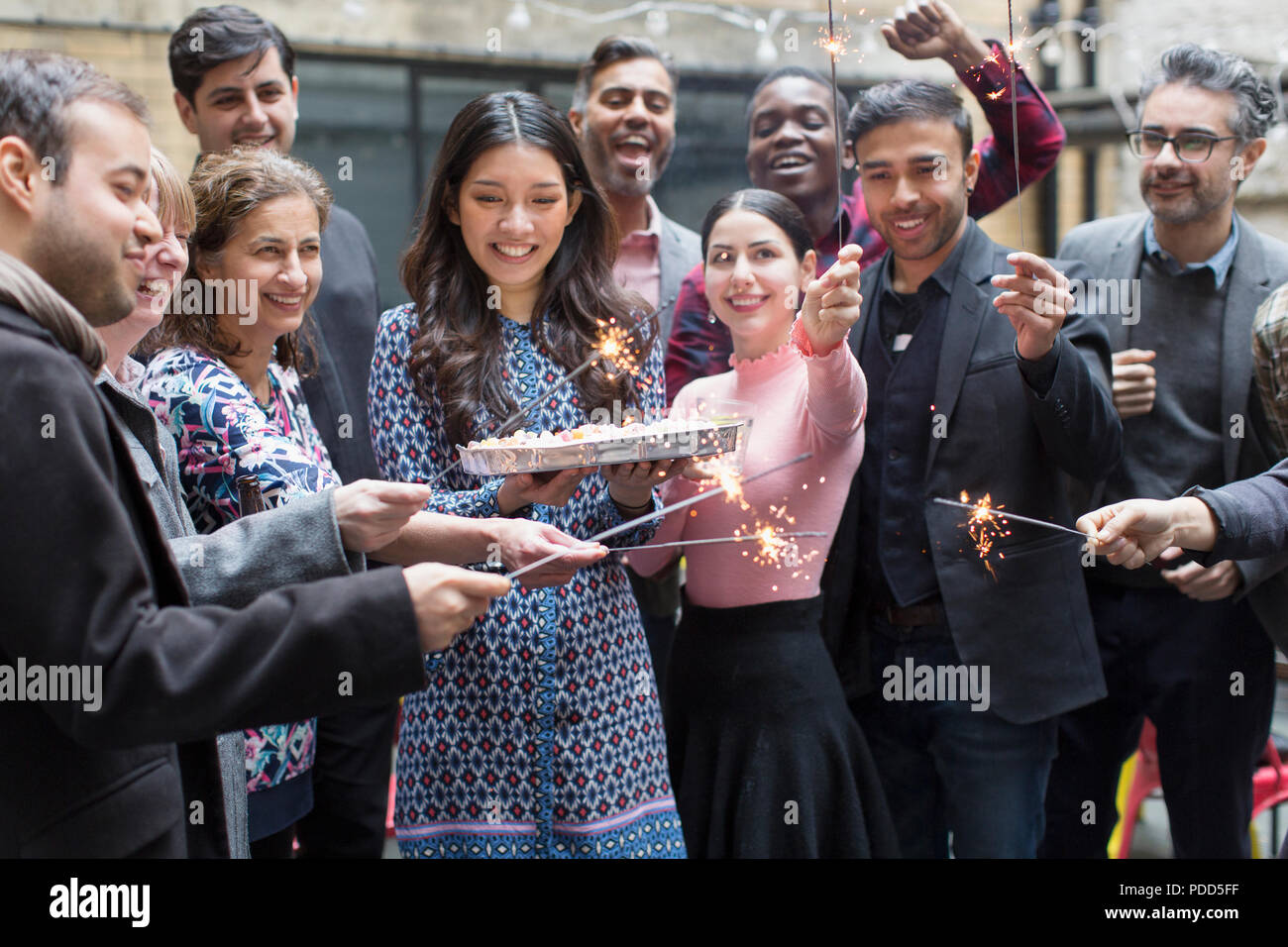 Friends with sparklers celebrating with woman holding birthday cake Stock Photo