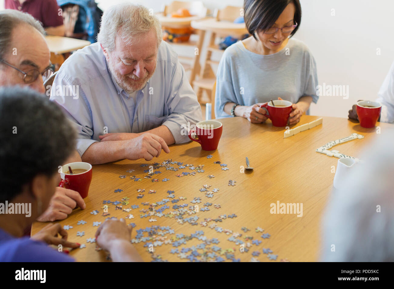 Senior friends assembling jigsaw puzzle and drinking tea at table in community center Stock Photo