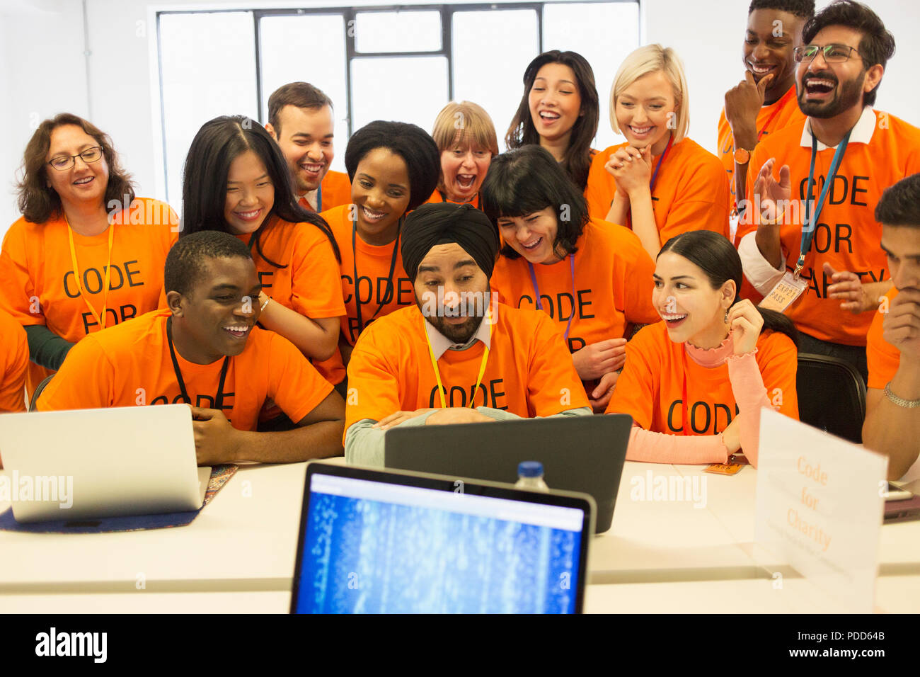 Happy hackers sharing laptop, coding for charity at hackathon Stock Photo