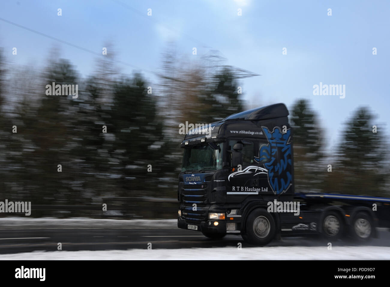 Scania truck pulling flatbed trailer on A road in Winter conditions Stock Photo