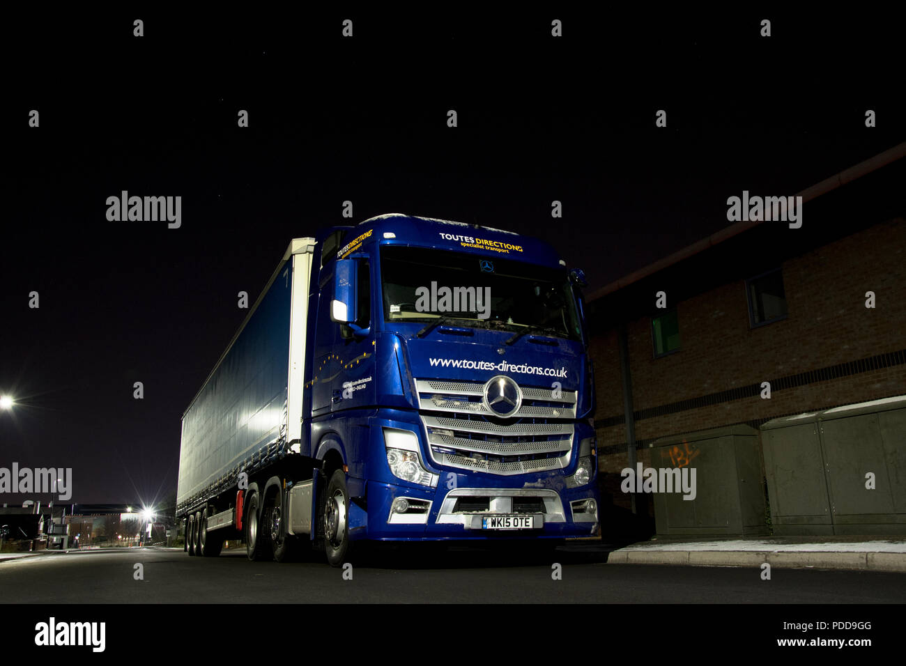 Mercedes Benz Actros pulling a steel container trailer makes a night delivery stop on an industrial estate Stock Photo