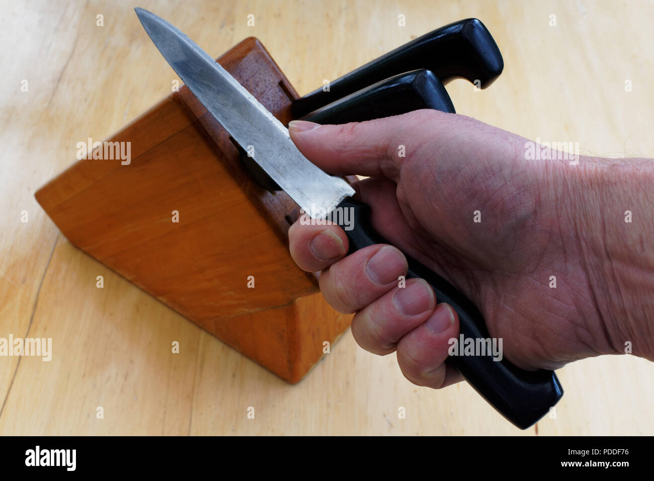 A hand holding a knife taken from a knife block and the thumb pressing on the blade to test its sharpness. It's not the sharpest knife in the block. Stock Photo