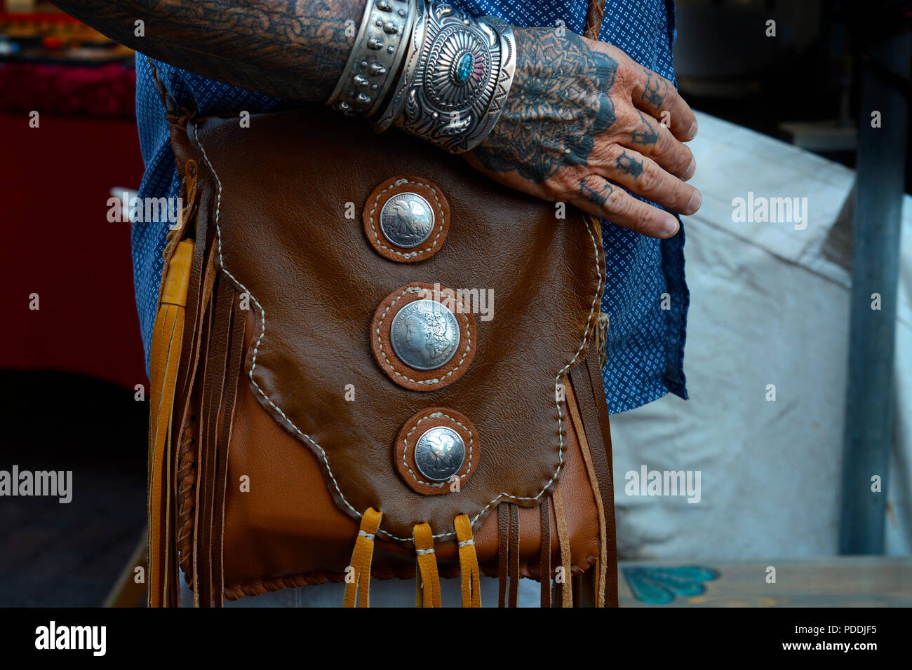 A man with tattooed arm and hand wearing  artist made jewelry and handmade leather bag. Stock Photo