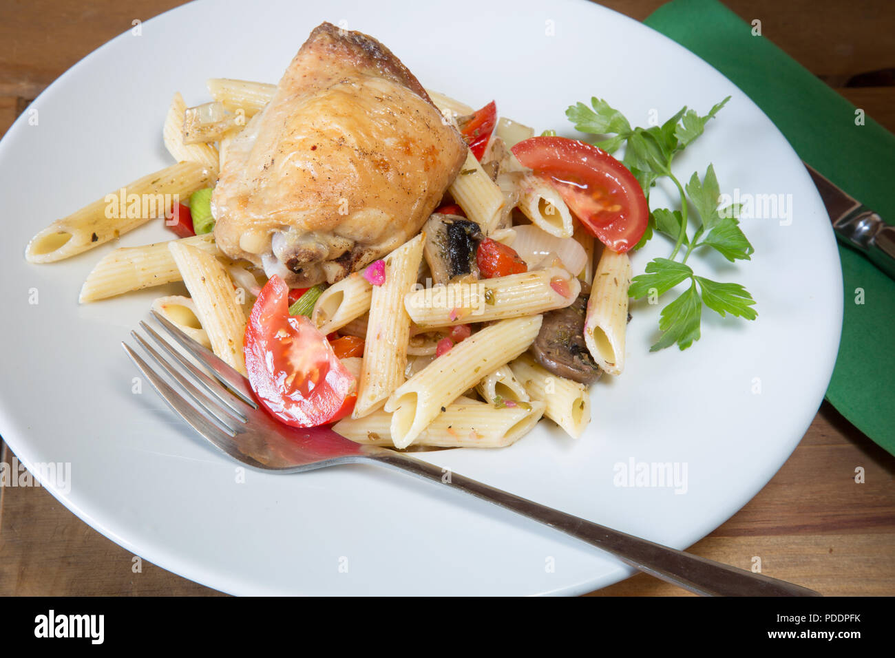 A plated meal of Pollo e Penne, Garlic infused roast Chicken thigh with Penne pasta and tomato, onion and mushroom Stock Photo