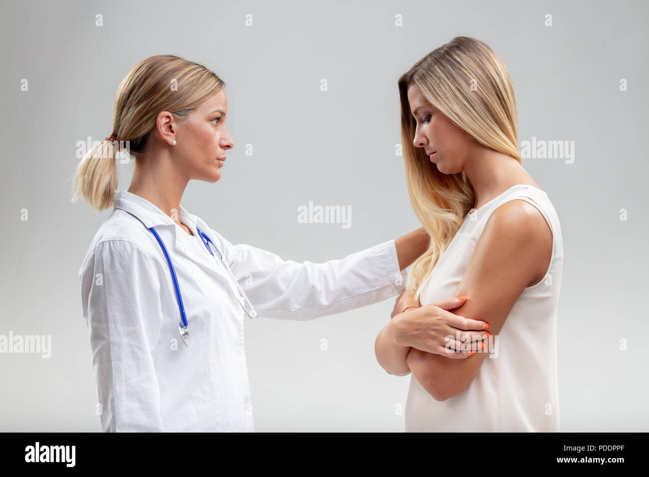 Serious woman doctor showing empathy for a young female patient reaching out a comforting hand to her shoulder in a close up side view Stock Photo
