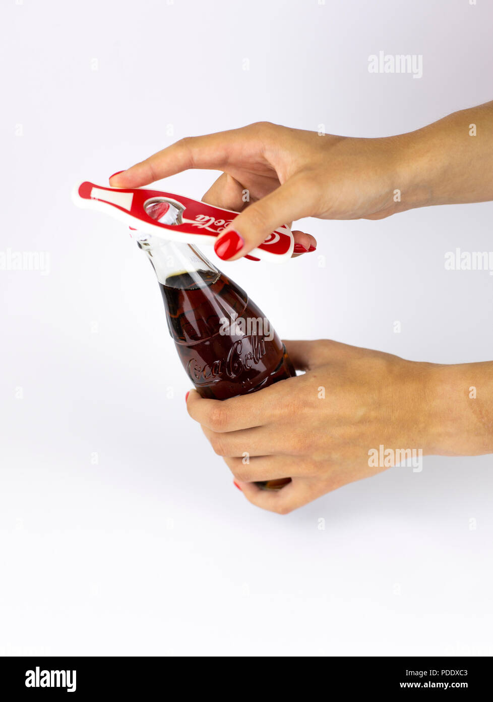 Atlanta, Georgia, USA - July 22, 2018: woman hand with red nails holding vintage historical embossed glass coca-cola contour classic bottle from USA on white background opening with red coca-cola brand opener Stock Photo
