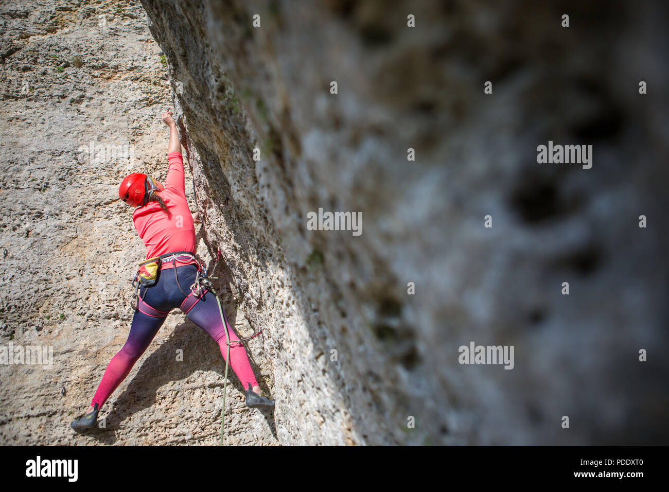 Photo of sports woman in red hard hat with carbine in hand climbing