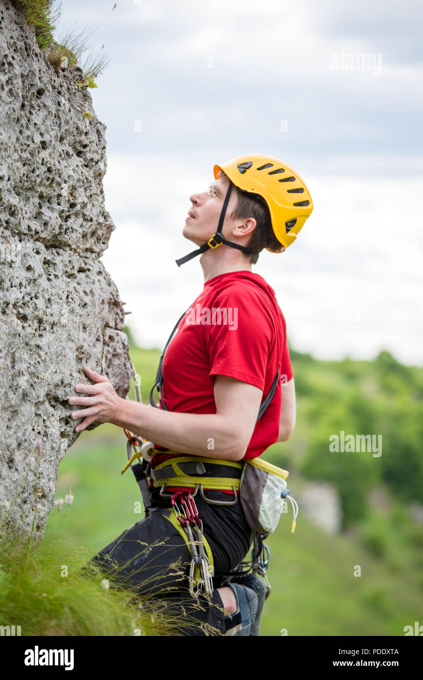 Photo of sportsman in yellow helmet clambering over rock against background of green trees Stock Photo