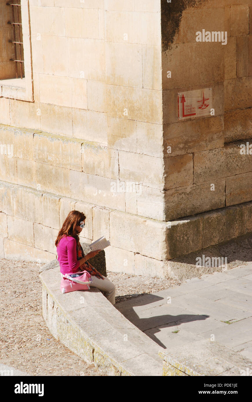 Woman reading a book, sitting on stone bench. Santo Domingo de Silos, Burgos, Spain. Stock Photo