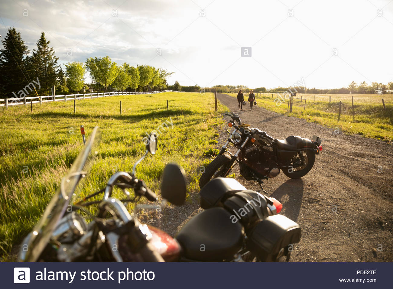 Women friends walking away from motorcycles on sunny rural road Stock Photo