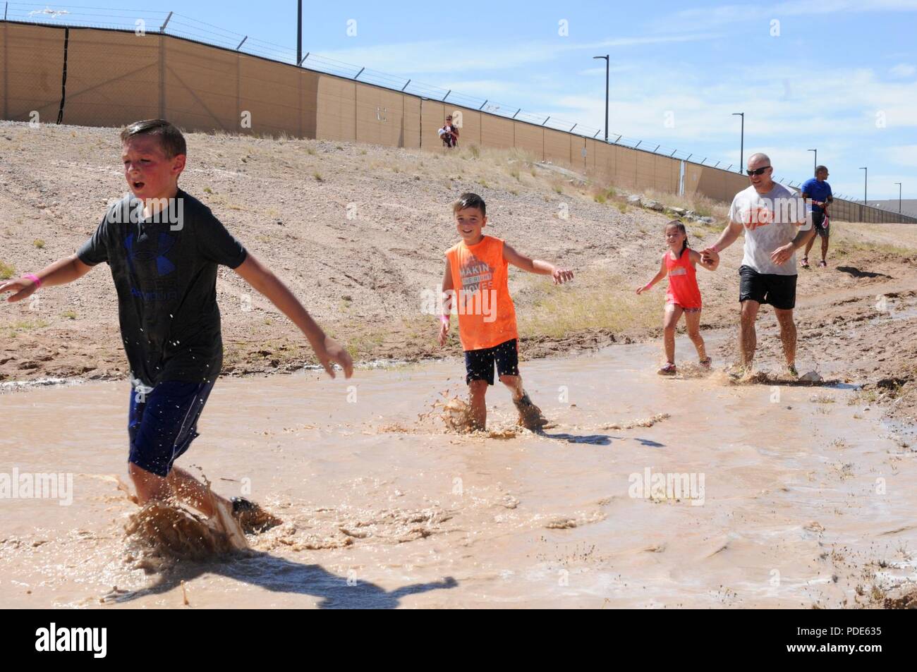 Participants of the Fort Bliss Old Ironsides Mud Challenge run through the water to cool off after the air assault obstacle course May 12, 2018 on Fort Bliss, Texas. The four-mile course was designed to promote physical fitness while also allowing the community to come together and have fun. Stock Photo