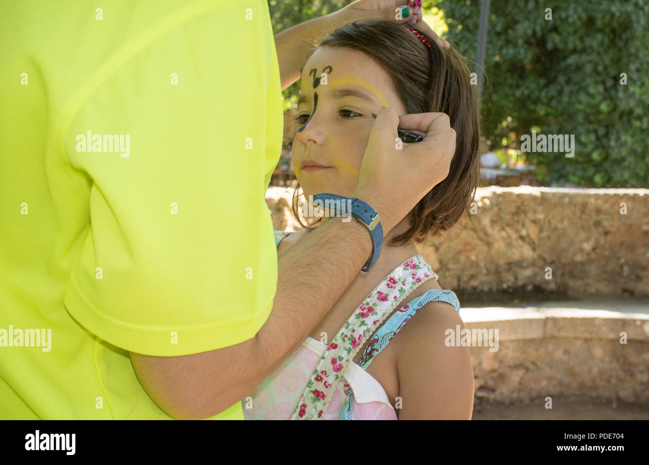 Little girl getting face painted during outdoors party. The make-up artist uses face paint crayons Stock Photo
