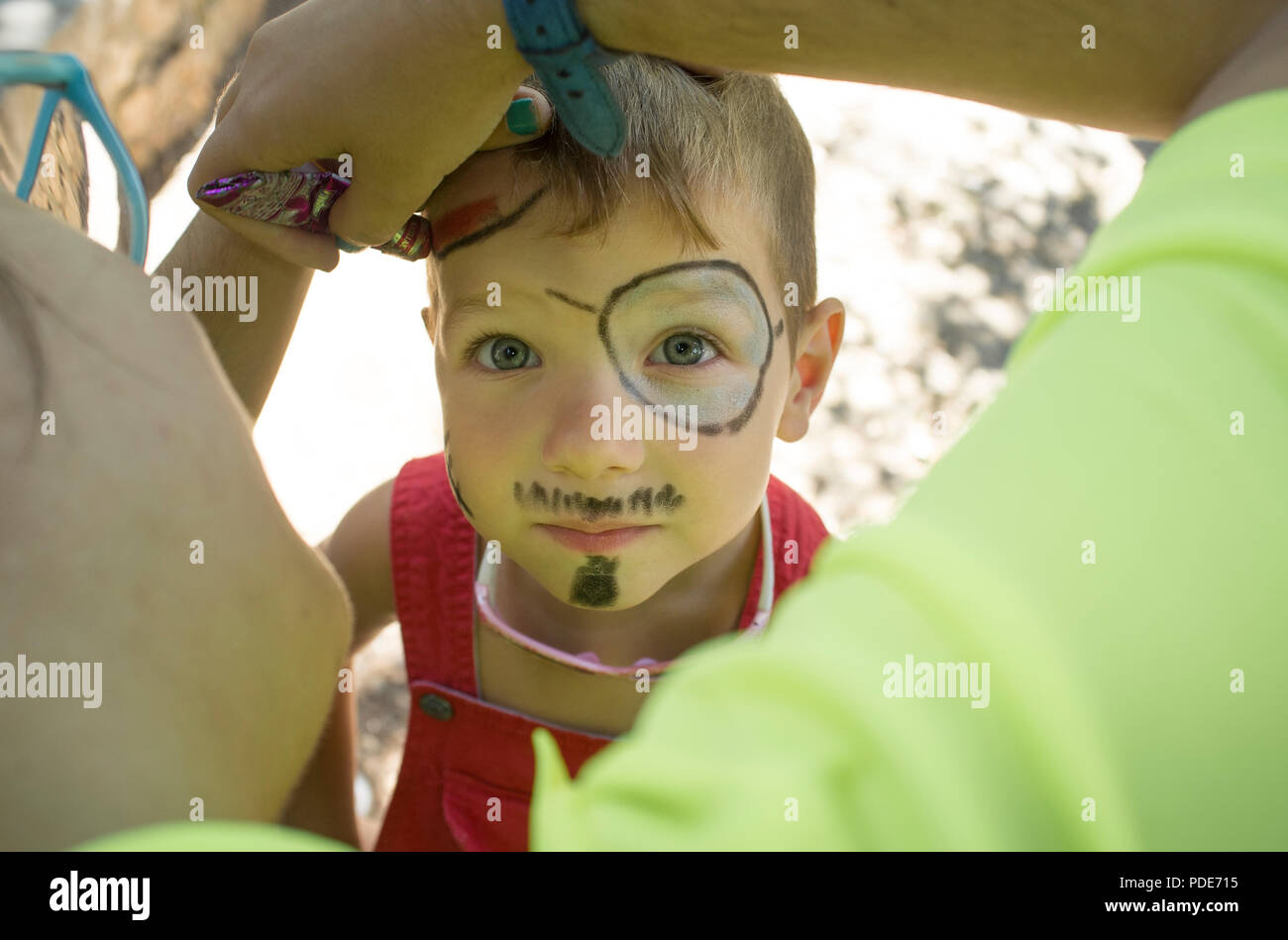 Little boy getting face painted during outdoors party. The make-up artist uses face paint crayons Stock Photo