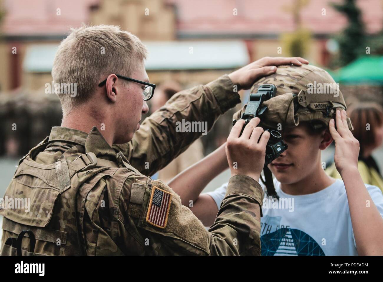 Pfc. Anothony Richardson, a Benton, Arkansas native and infantryman with 1st Squadron, 2nd Cavalry Regiment, puts his Kevlar helmet onto a Polish citizen during an event to celebrate the anniversary of the polish boarder guard with Battle Group Poland at Ketrzyn, Poland on May 18, 2018. Battle Group Poland is a unique, multinational coalition of U.S., U.K., Croatian and Romanian Soldiers who serve with the Polish 15th Mechanized Brigade as a deterrence force in support of NATO’s Enhanced Forward Presence. Stock Photo