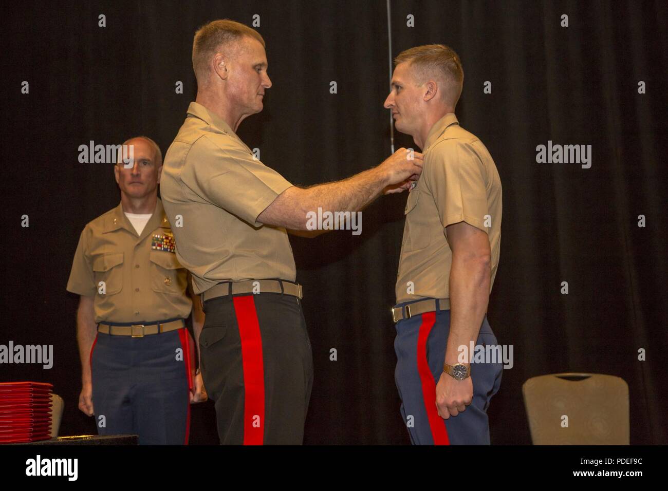 The deputy commandant for aviation, Lt. Gen. Steven R. Rudder, Headquarters Marine Corps, center, presents the Unmanned Aerial System officer insignia to Capt. Joshua P. Brooks, an unmanned aircraft commander with Marine Unmanned Aerial Vehicle Squadron (VMU) 3, 1st Marine Aircraft Wing, during the 2018 Marine Corps Aviation Association Winging Ceremony held in San Diego, May 18. Awarding of this insignia adds to the distinguished legacy of the Marine Corps’ longstanding tradition of pioneering aviation excellence while setting the standard for advancing remote combat operations and warfightin Stock Photo