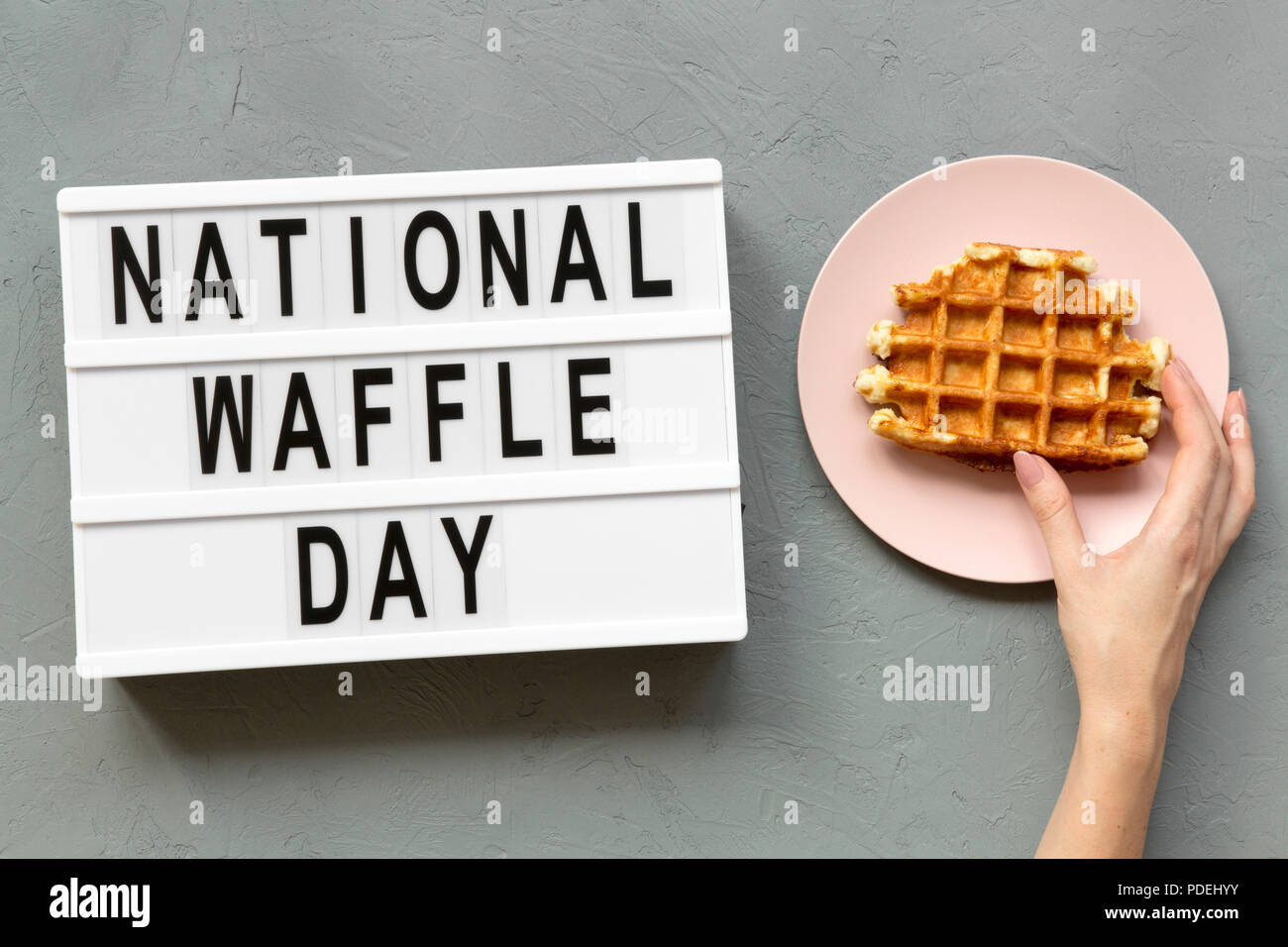 'National Waffle Day' word on lightbox, female hand takes traditional