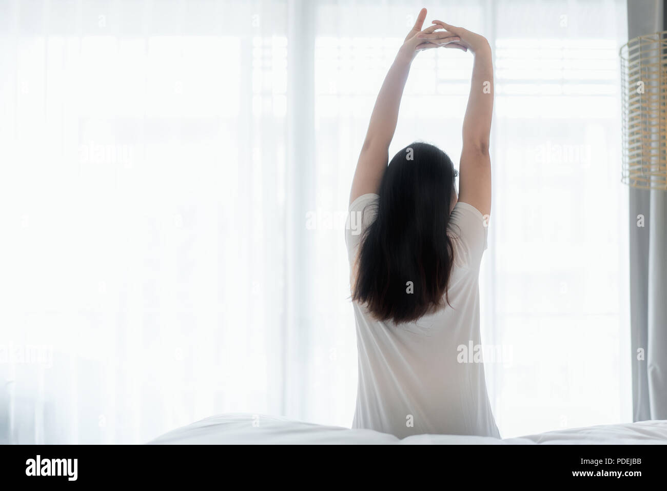 Asian Woman stretching in bed after wake up in bedroom at home, back view Stock Photo