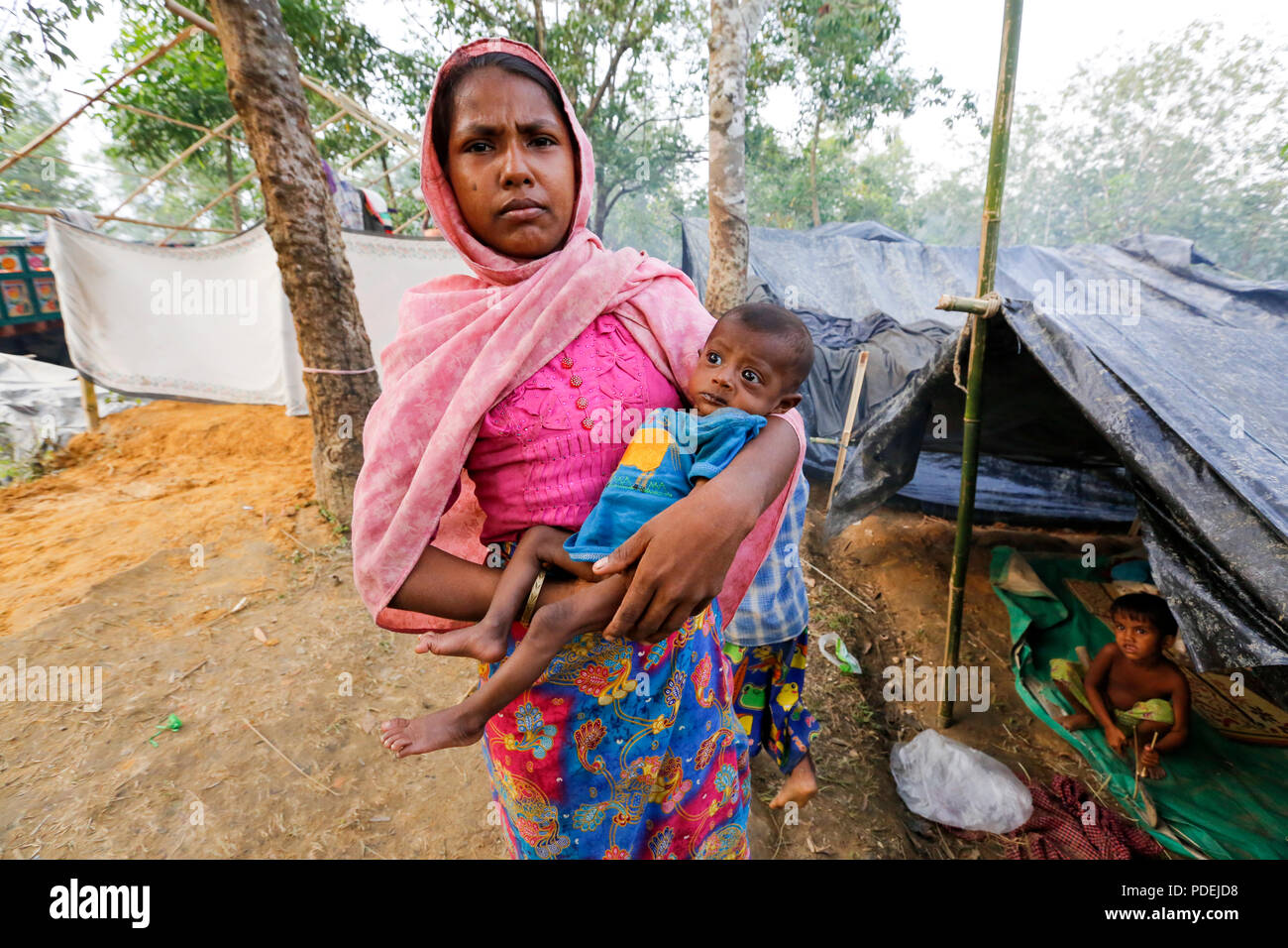 A Rohingya mother along with her child stands in front of her makeshift at Kutupalong Refugee Camp. Cox's Bazar, Bangladesh Stock Photo