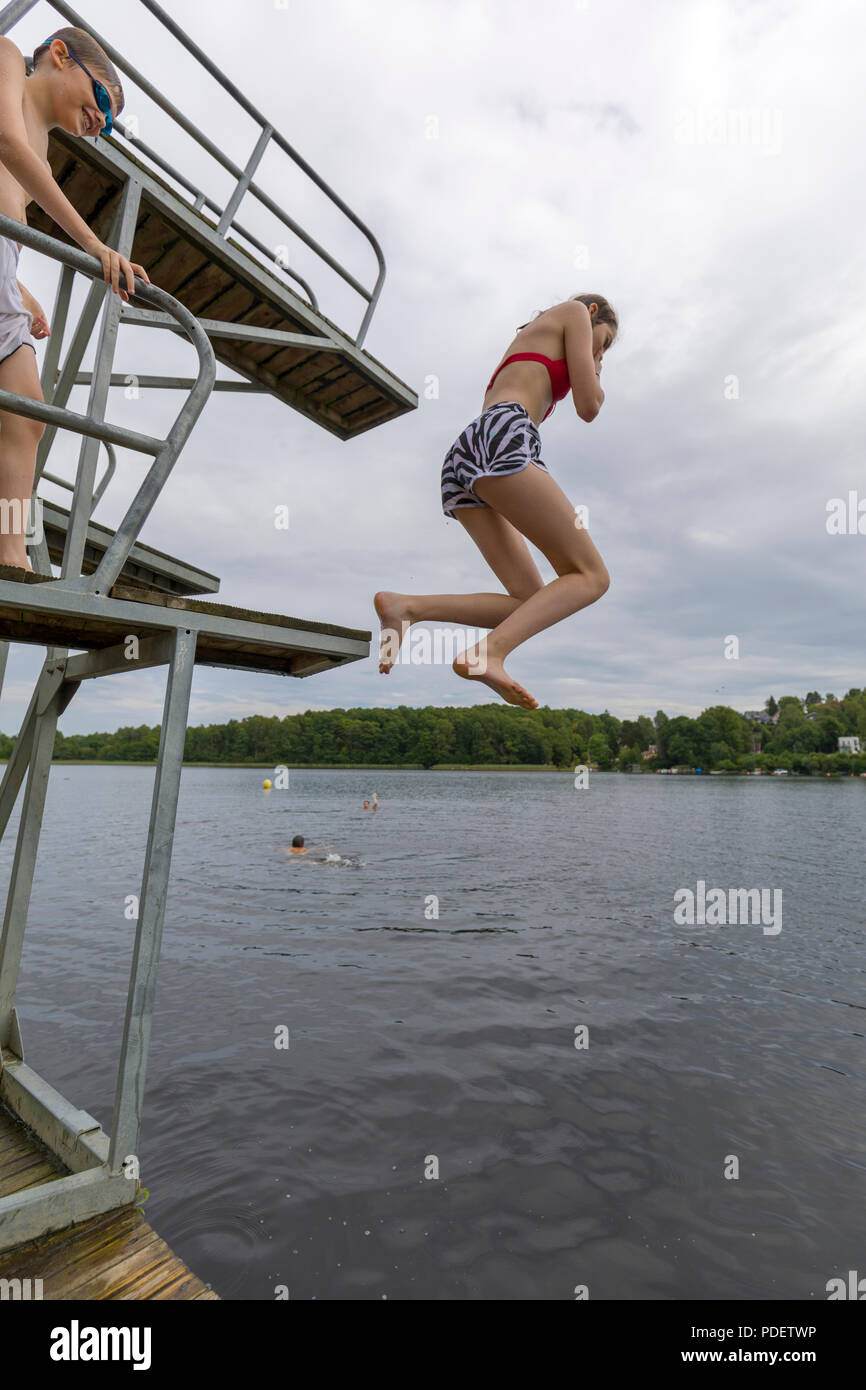 Teenage girl jumping into lake water from jetty jumping tower holding her nose Stock Photo