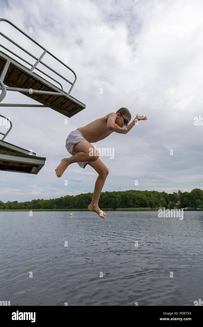 10 year old boy jumping into lake water from jetty jumping tower holding his nose Stock Photo