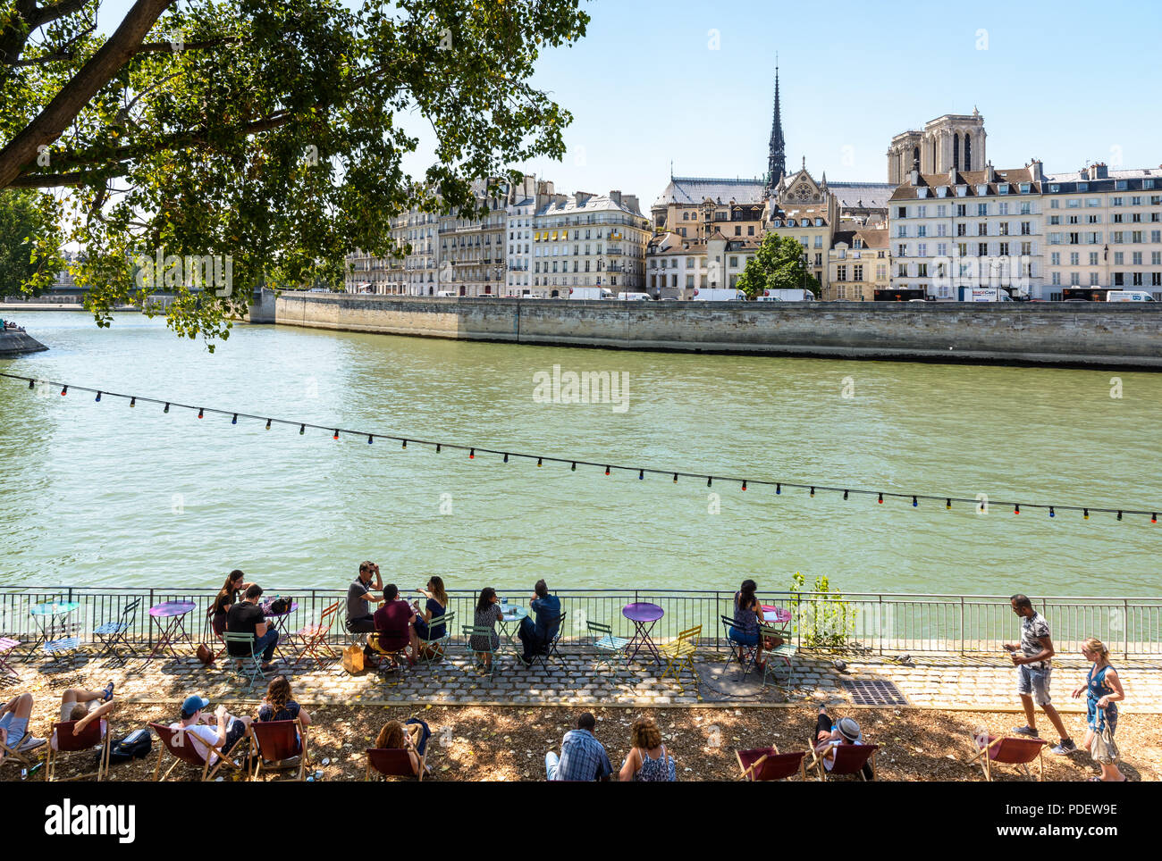 People resting on deck chairs along the Seine during Paris-Plage summer event in Paris, France, with Notre-Dame de paris cathedral in the background. Stock Photo