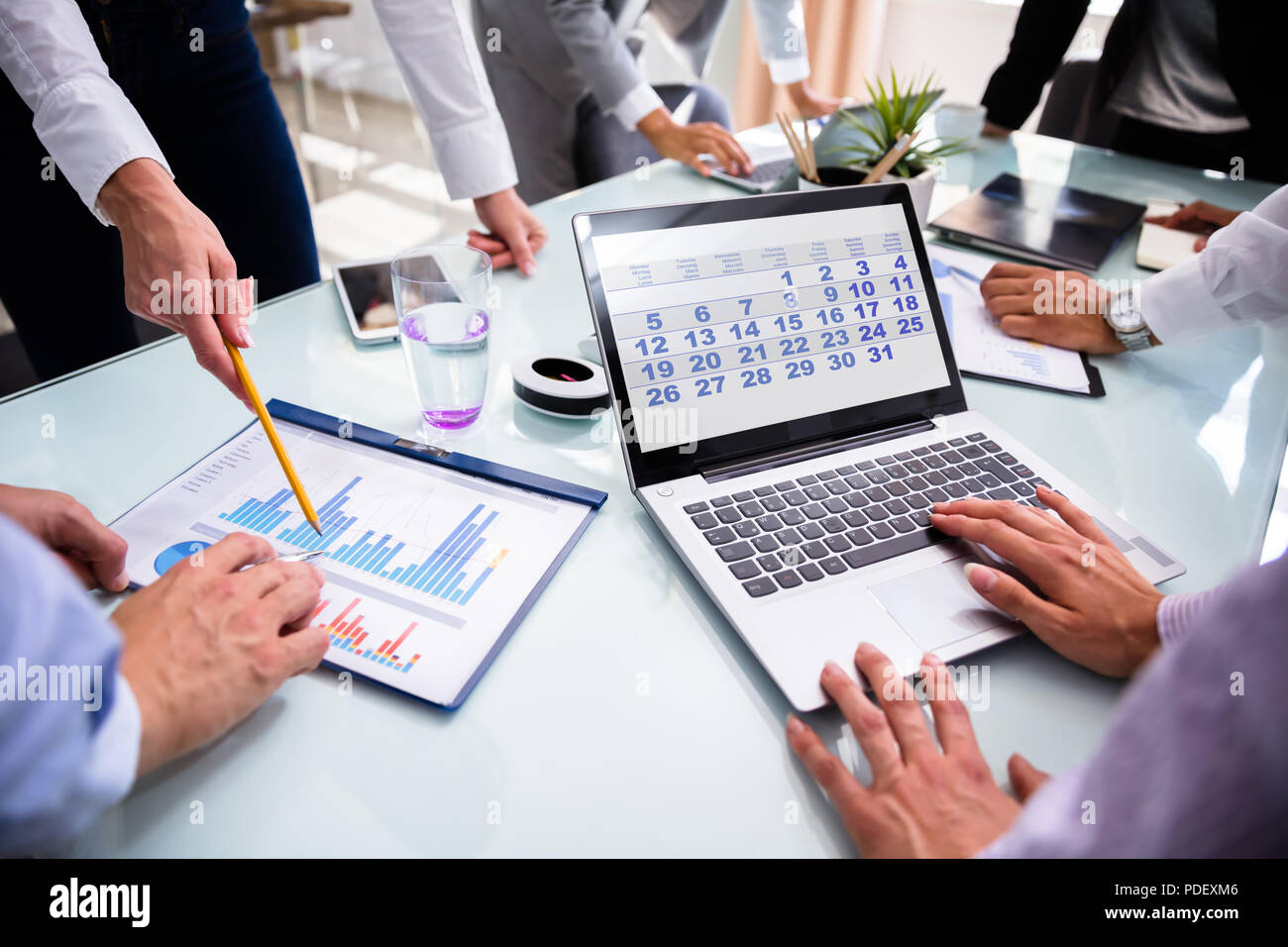 Businesspeople Using Calendar On Laptop While Analyzing Graphs Over Desk Stock Photo