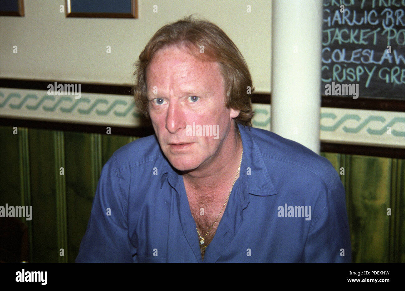 Dennis Waterman sitting in pub restaurant wearing blue shirt Stock Photo