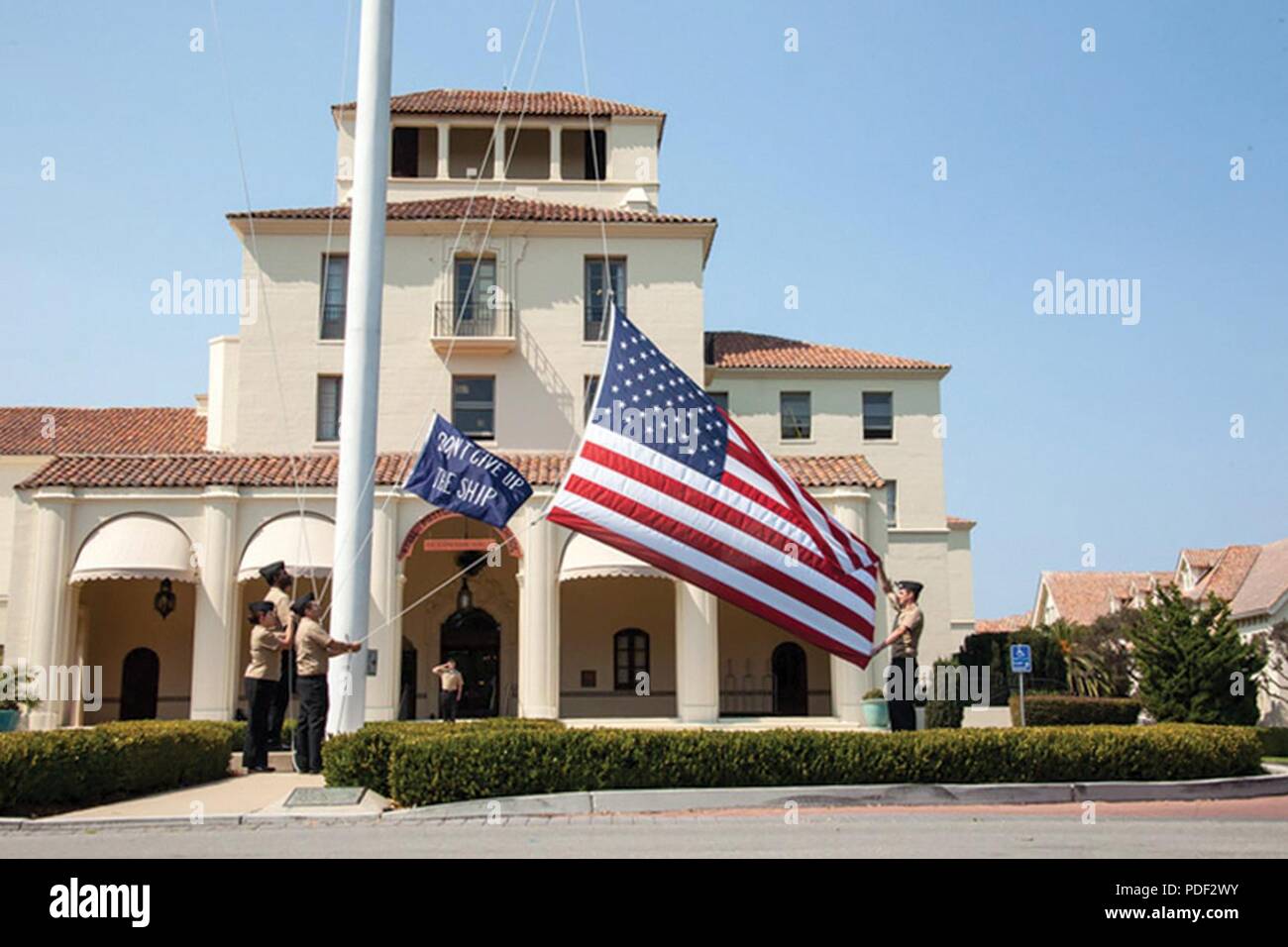 Sailors raise a pennant that reads “Don’t give up the ship” during morning colors in front of NPS’ Herrmann Hall. NPS is now offering new curricula in systems and program management and in systems engineering management to students from the Army Acquisition Workforce. Stock Photo