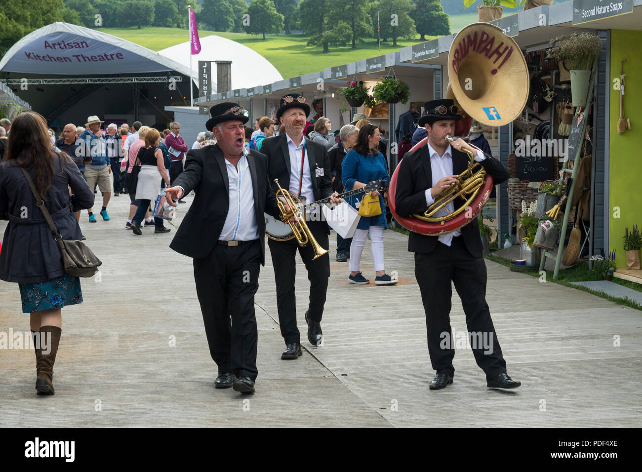 Male trio of lively musicians entertaining people, playing & walking on  avenue of trade stands - RHS Chatsworth Flower Show, Derbyshire, England, UK Stock Photo