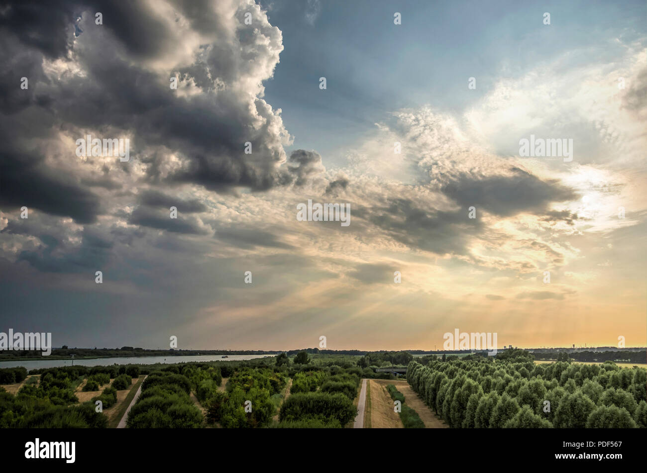 Dramatic skies with low sun and dark clouds approaching over the island of IJsselmonde and the Oude Maas river as seen from the artificial hill at Car Stock Photo