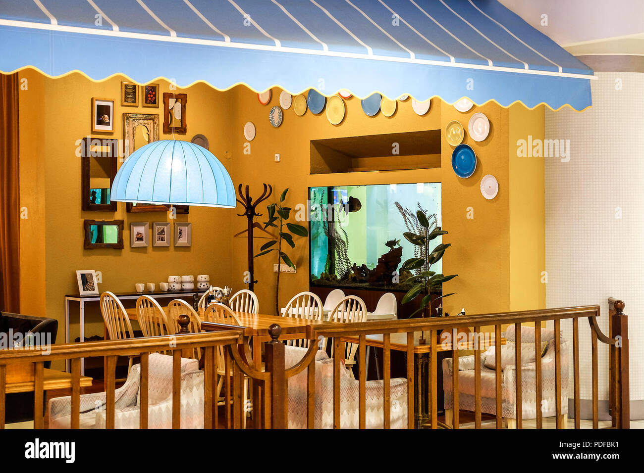 It is an Italian restaurant with a traditional interior. Blue canopy of awnings for shade. Lamp with blue lampshade above the table. Stock Photo